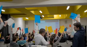 Lidé na zasedání zvedají ruce s hlasovacími lístky.