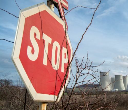Dopravní cedule STOP a v pozadí chladící věže elektrárny.
